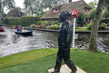 a statue of a man walking on grass next to giethoorn canal with holland experience tour