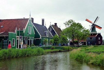 a river with a green house and a windmill